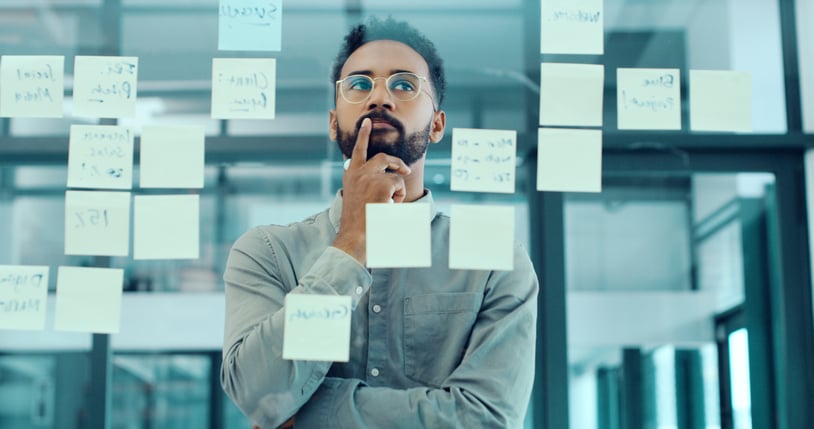man standing in front of window and post it notes thinking